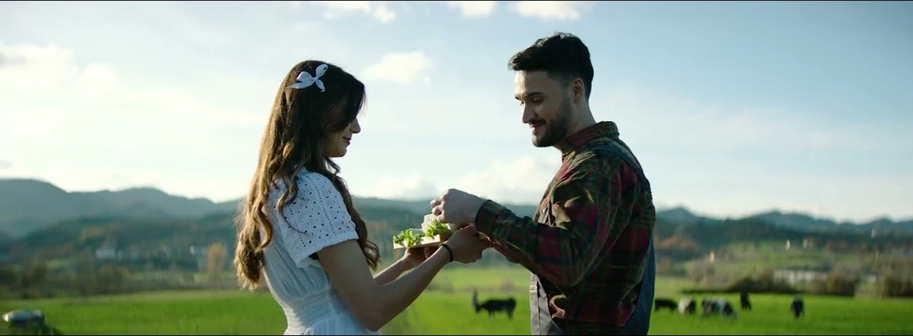 A couple holding a drink in a sunlit mountain landscape