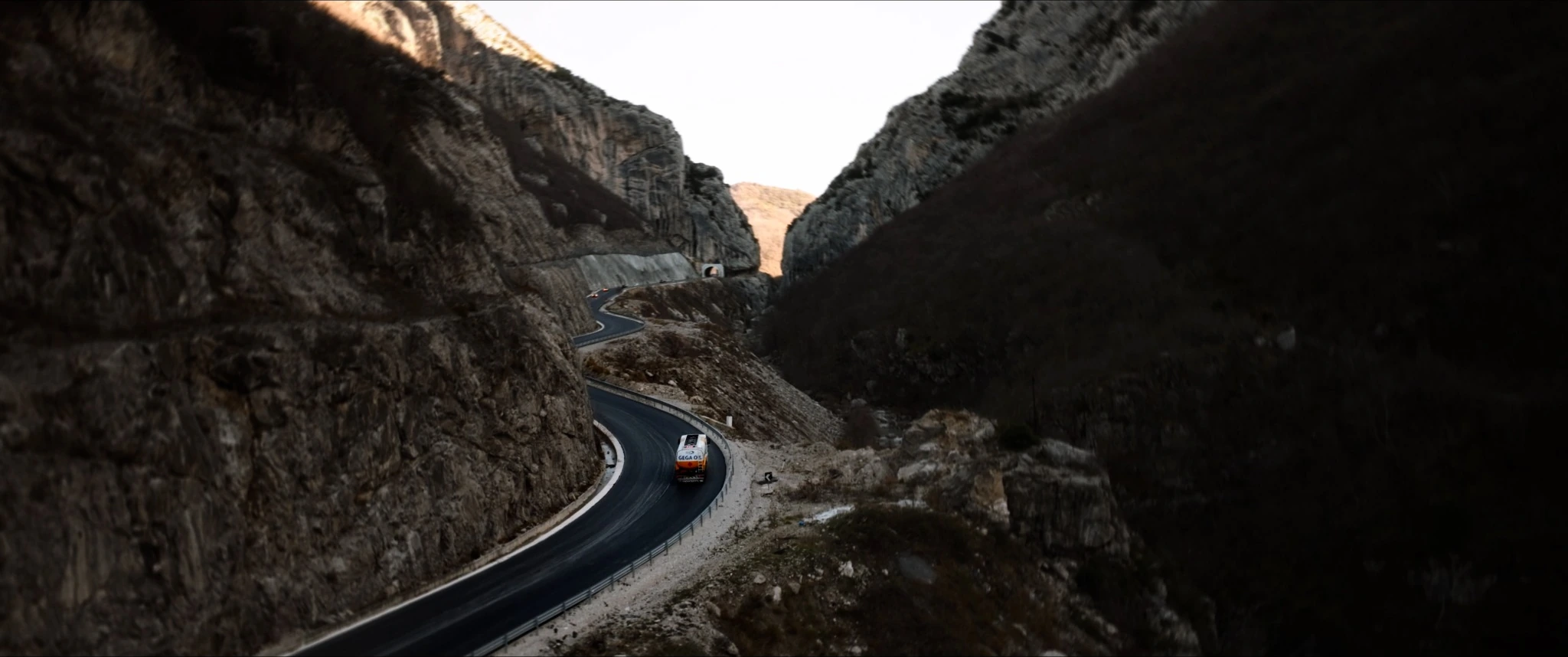 A Gega Oil truck on a winding road through a rocky mountain gorge